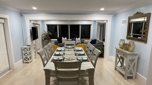 Un espace repas avec une longue table dressée pour six personnes, entourée de chaises.