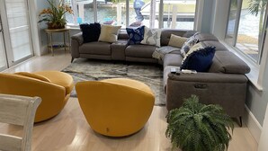Un salon moderne avec un canapé d’angle, des fauteuils jaunes et une grande fenêtre donnant sur un port de plaisance.