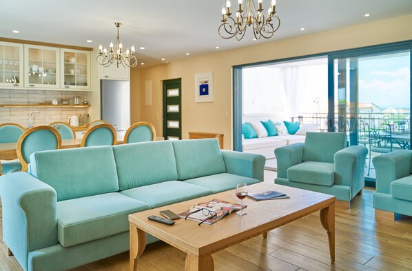 A spacious living area with a light blue sofa, matching armchairs, and a wooden coffee table. A chandelier hangs from the ceiling, and a large window offers a view of the outdoors. - Luxury Villa Indigo with Pool (Split)