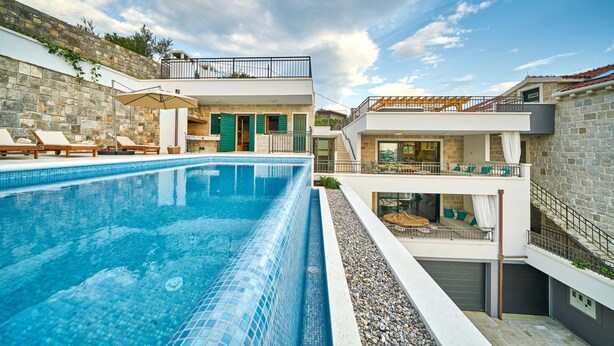 A modern pool area with a clear blue pool, lounge chairs, and a stone wall. - Luxury Villa Indigo with Pool (Split)