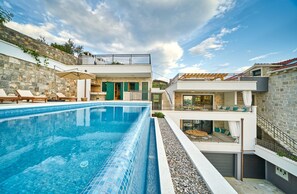 Et moderne poolområde med en klar blå pool, liggestole og en stenvæg.