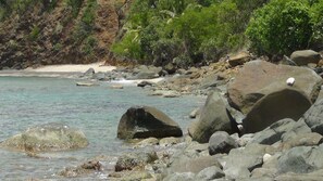 A rocky shoreline with clear water, large boulders, and a sandy beach.