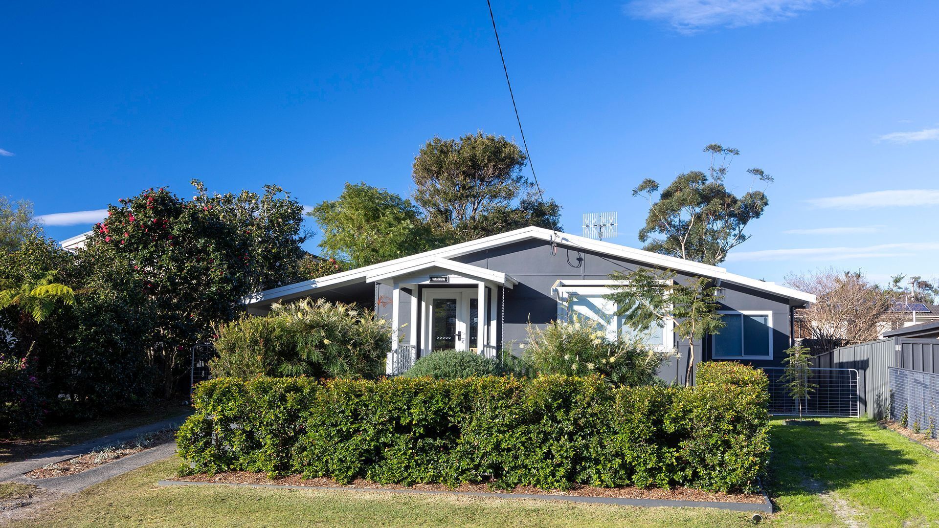 A modern two-story house with a covered porch, surrounded by lush greenery and trees.