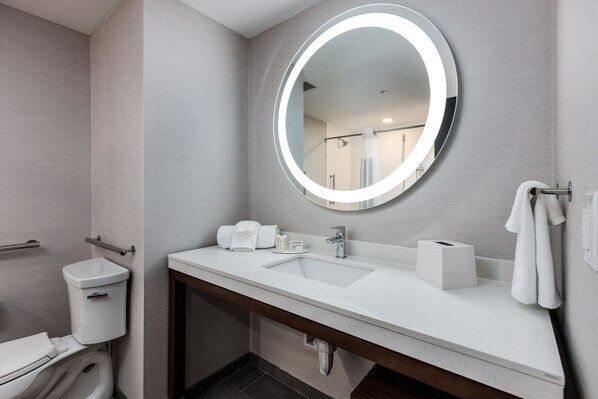 A modern bathroom with a white sink, a round mirror with a light, a toilet, and a towel rack.