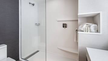 Een moderne badkamer met een douchecabine van glas, een wit toilet en een inbouwplankje met handdoeken.