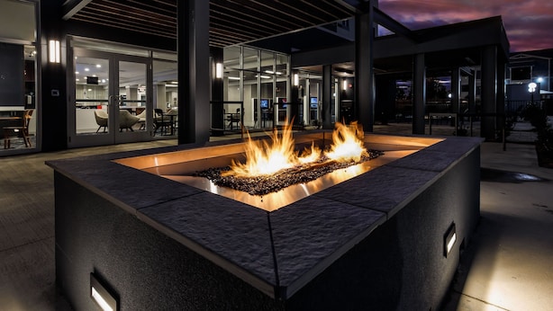 A modern outdoor fire feature with a glass enclosure, surrounded by a contemporary building with large windows and a flat roof.
