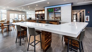 A modern bar area with a long white counter, bar stools, and a television screen displaying sports.