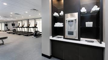 A gym with treadmills, a water dispenser, and neatly folded towels on shelves.