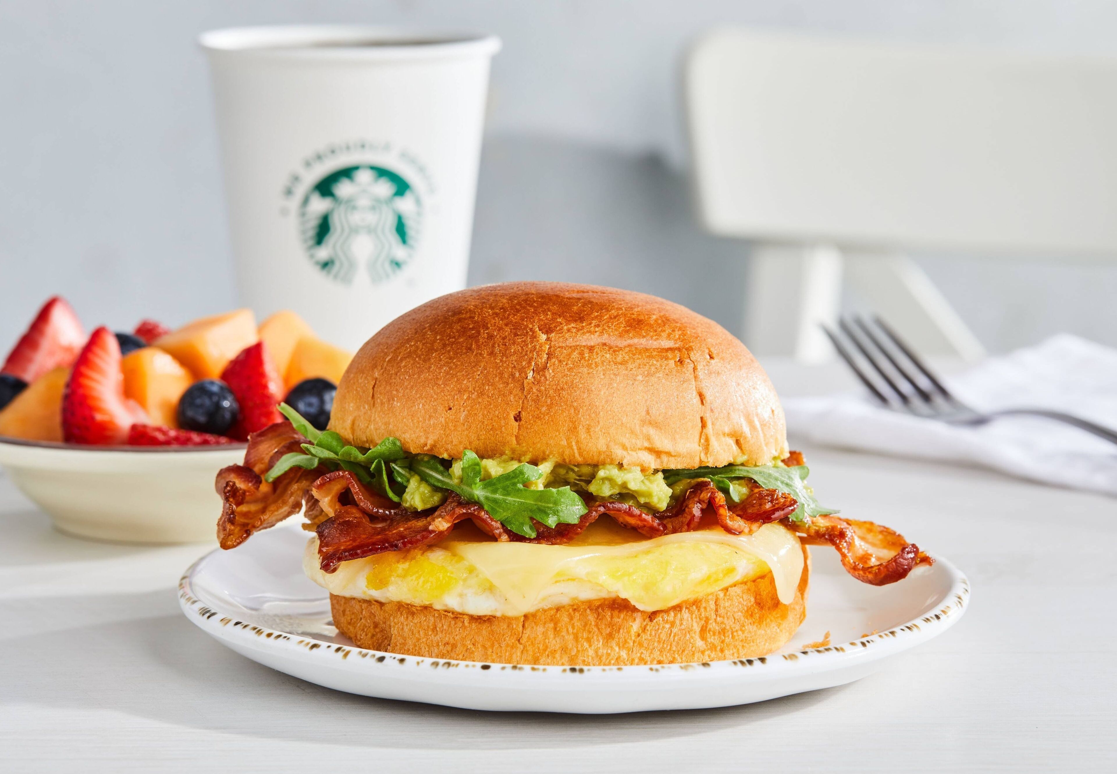A breakfast sandwich on a plate with a Starbucks cup in the background.