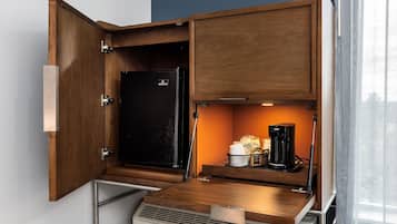Una kitchenette compacta con nevera integrada, cafetera y una pequeña encimera.