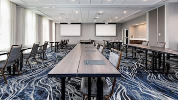 Un salón de conferencias con una larga mesa, varias sillas, una pantalla de proyector y suelo alfombrado.