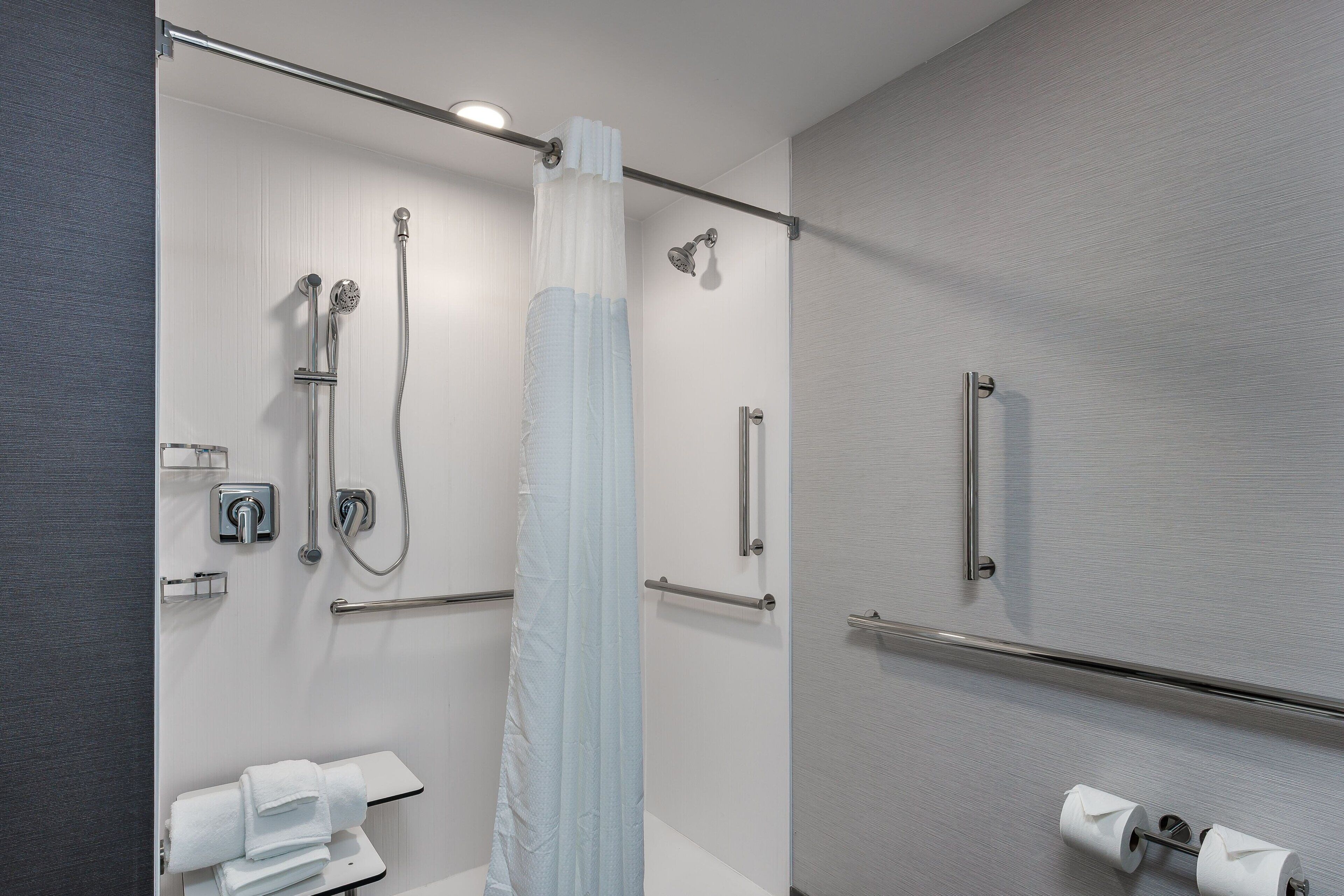 Een moderne badkamer met een douchecabine van glas, een handdoekhouder en een toiletpapierhouder.