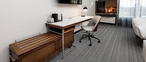 Habitación de hotel con escritorio, silla, cama, televisión y vistas al exterior.