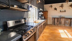 A kitchen with a stainless steel stove, wooden cabinets, and a window. - The Dam Ranch · The Dam Ranch | Country Living + Modern Amenities (New Braunfels)