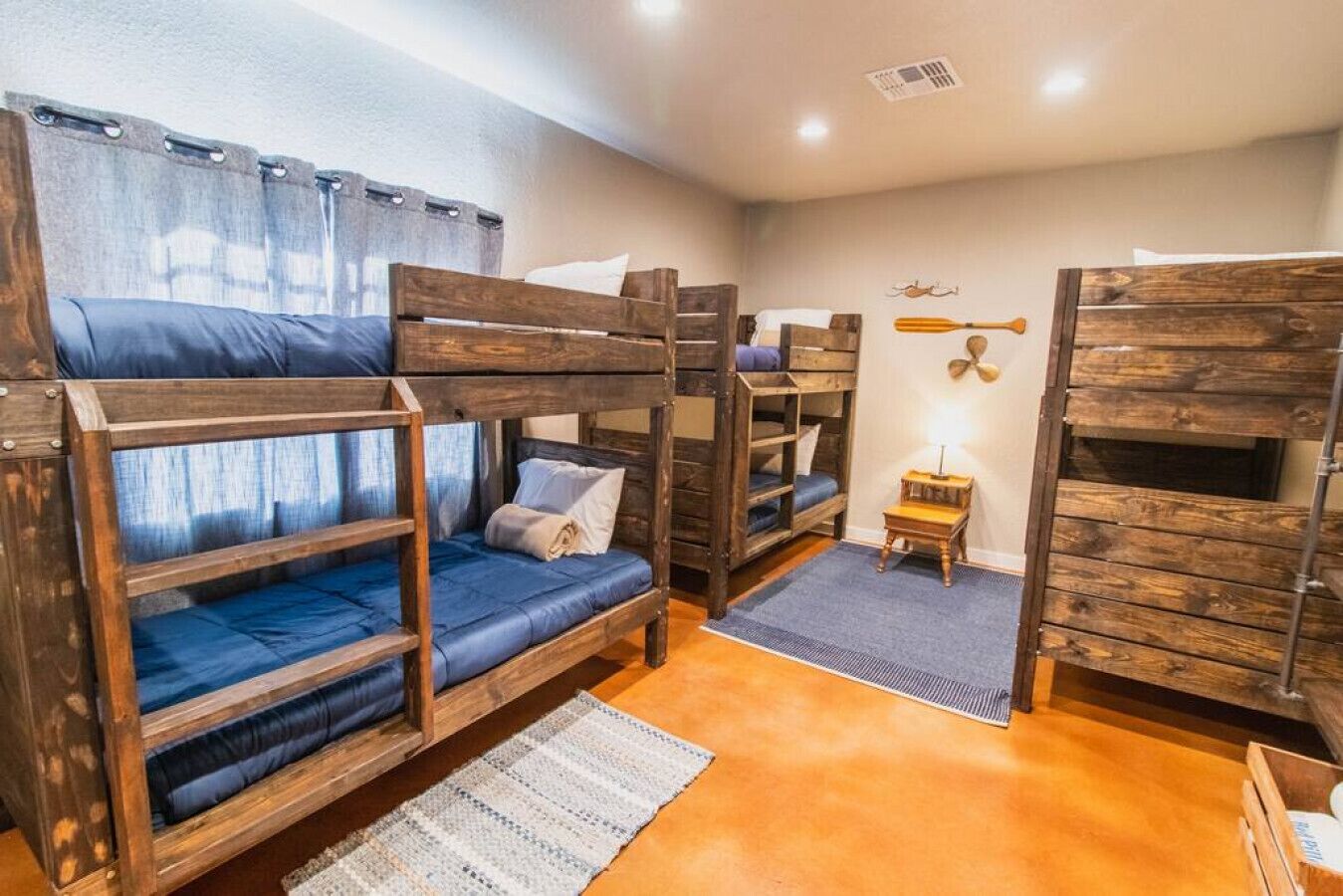 A bunk bed room with wooden bunk beds, a small table, and a wall-mounted fan.