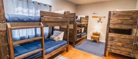 A bunk bed room with wooden bunk beds, a small table, and a wall-mounted fan.