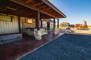 Un espacio al aire libre techado con una pared de piedra, una cubierta de madera y un molino en el fondo.