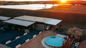 A lodge with a swimming pool, outdoor seating, and a view of a lake at sunset. - The Dam Ranch · The Dam Ranch | Country Living + Modern Amenities (New Braunfels)
