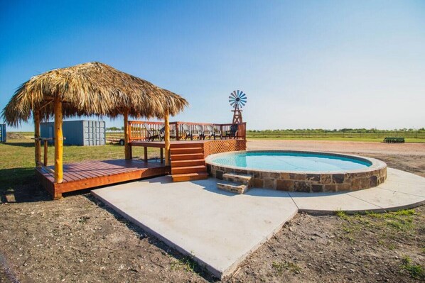 Un área de piscina con cubierta de madera, una estructura de techo de paja y un molino.