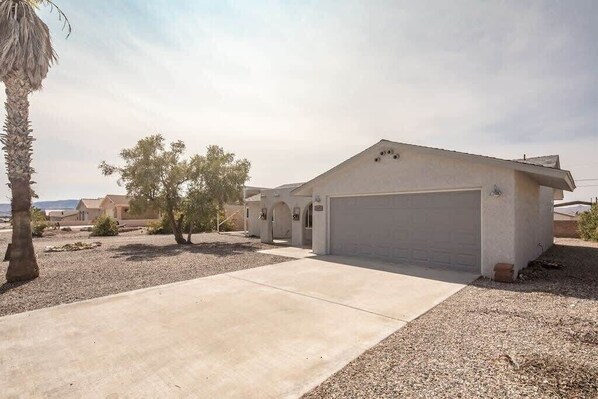 A single-story house with a garage, a driveway, and a small garden with a palm tree and shrubs.