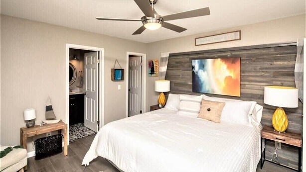 Una camera da letto con un letto grande, un ventilatore a soffitto, una testiera in legno e un quadro appeso al muro.