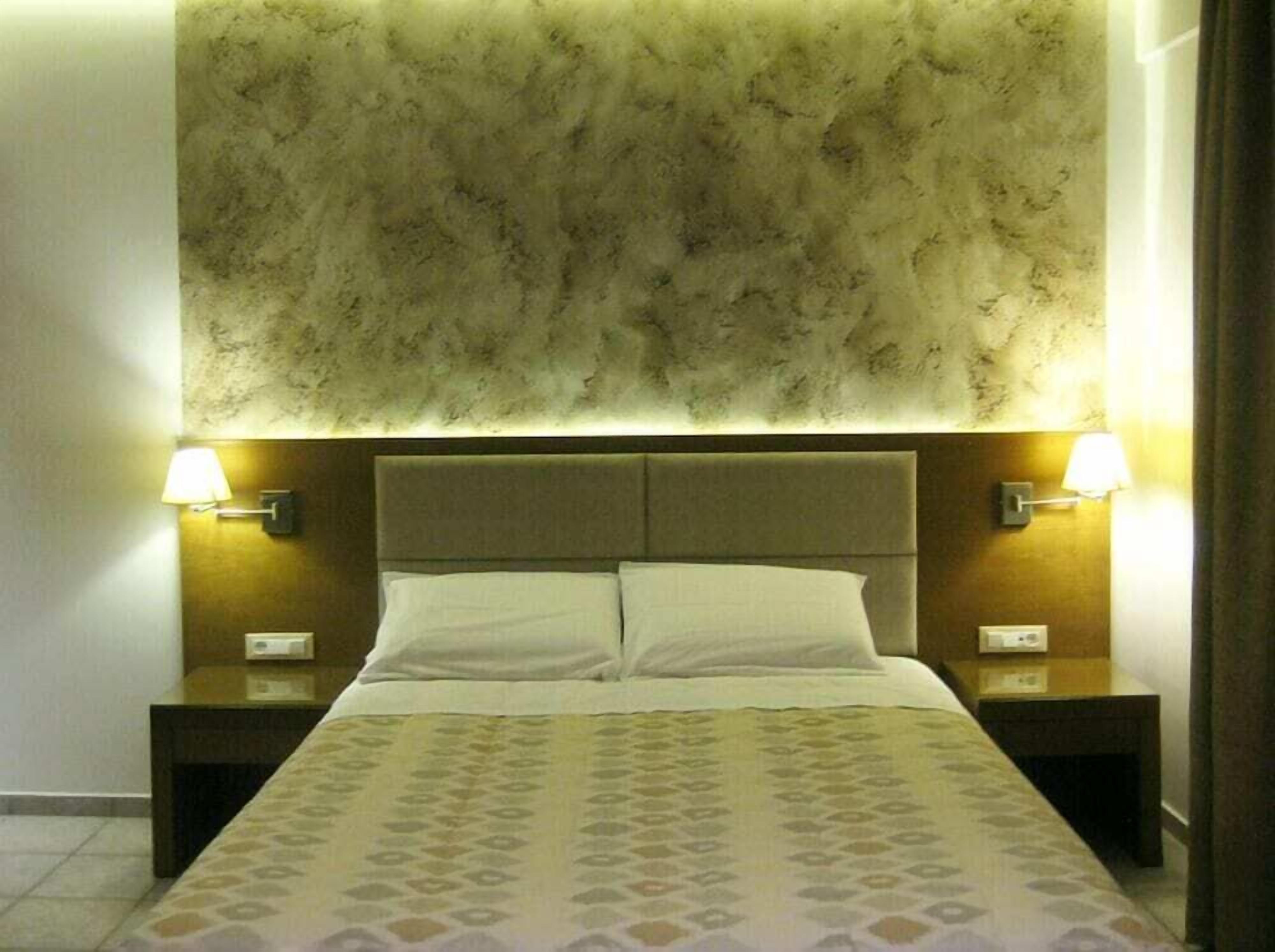 A hotel room with a large bed, two bedside tables, and a textured wall above the bed.