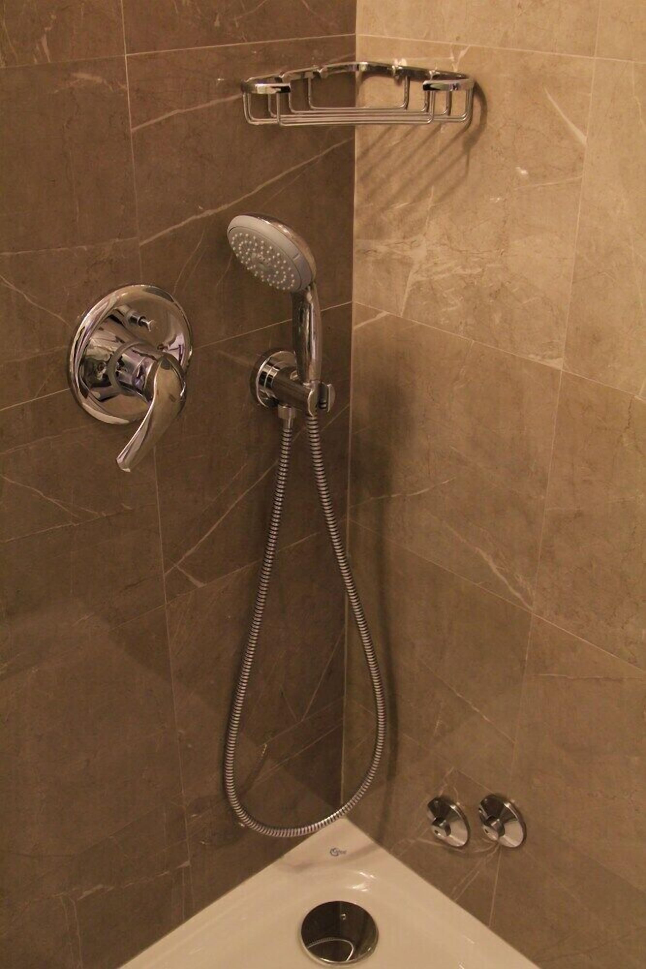 A bathroom with a shower, a handheld showerhead, a wall-mounted faucet, and a towel rack.