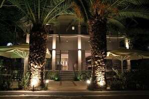 A building with a covered entrance, palm trees, and outdoor seating. - Achilles Hotel (Pylos-Nestoras)