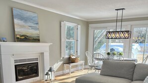 A living room with a fireplace, a sofa, a dining table with chairs, and a hanging light fixture. - Secluded Cottage Getaway (Saugatuck)