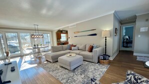 A spacious living room with a large sectional sofa, a patterned armchair, and a dining area with a glass table. - Secluded Cottage Getaway (Saugatuck)
