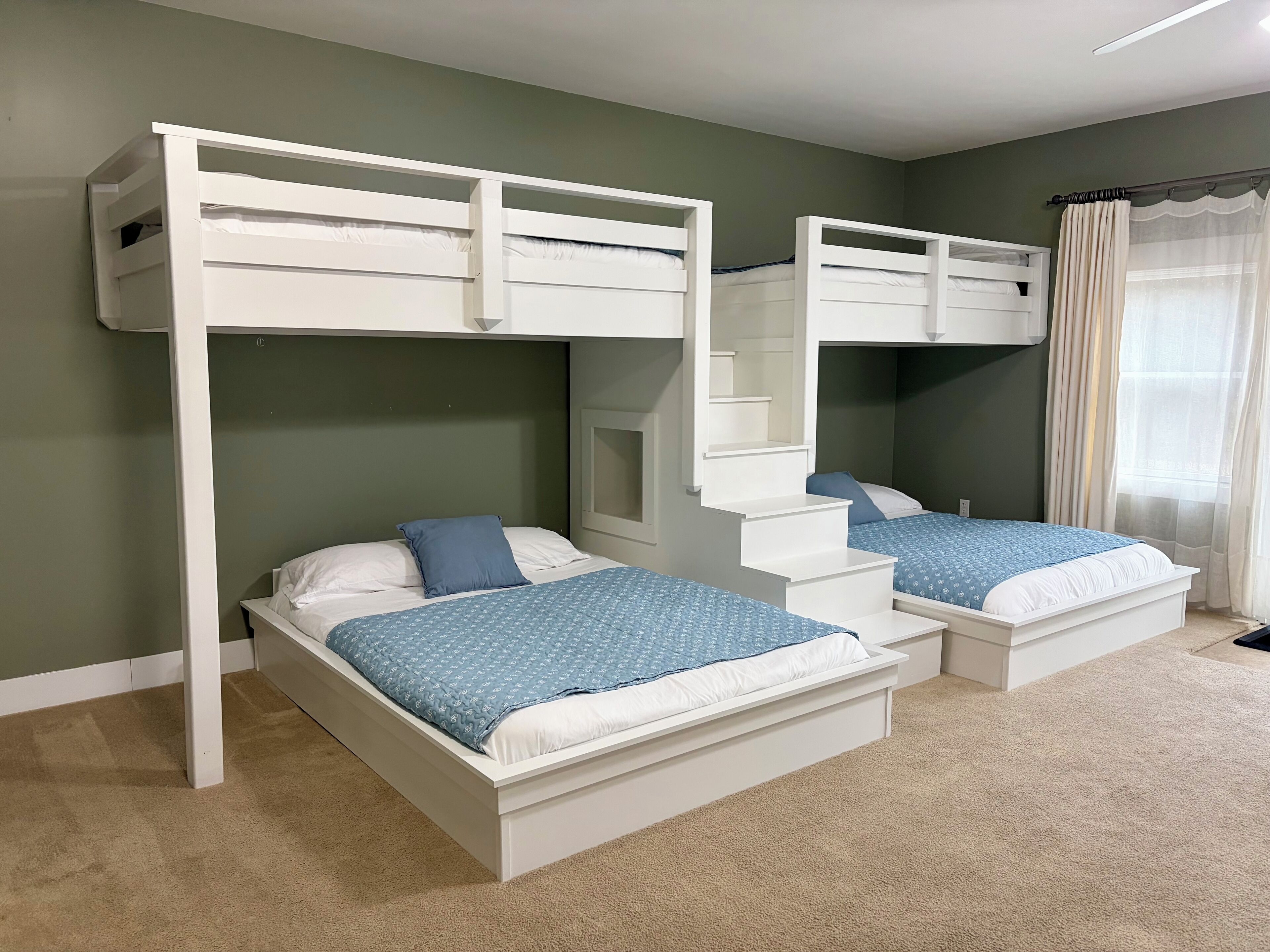 A room with two bunk beds, carpeted floor, and a window with curtains.
