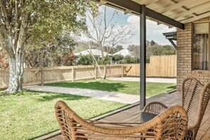 A covered patio with wicker furniture, a brick wall, and a wooden fence in the background. - Prowse Beach House—Family Fun & Ocean Adventures (Dunsborough)