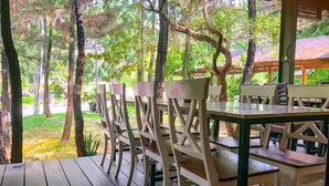 An outdoor wooden deck with tables and chairs, surrounded by trees and greenery. - New Green Sentul Resort (Sentul City)