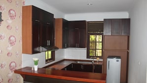 A compact kitchen with dark wooden cabinets, a white countertop, and a small refrigerator. - New Green Sentul Resort (Sentul City)