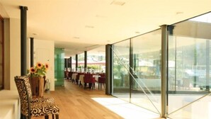 Ein modernes Interieur mit Holzboden, einer Essecke mit roten Stühlen und großen Glasfenstern.