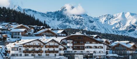 A snow-covered mountain resort with multiple chalet-style buildings, a ski lift, and a clear view of the surrounding mountains.