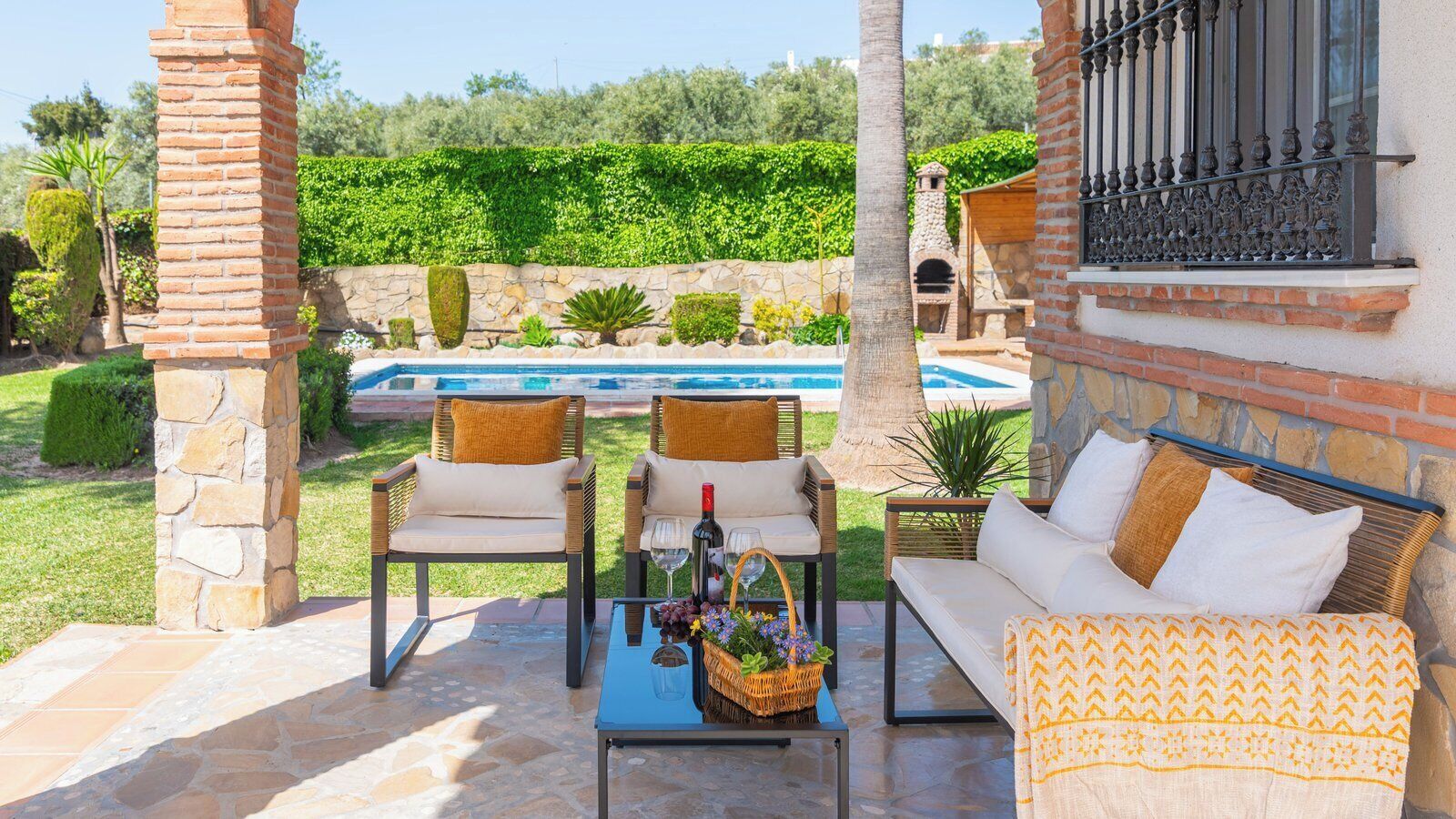 An outdoor seating area with a pool in the background, stone pillars, and a stone oven.