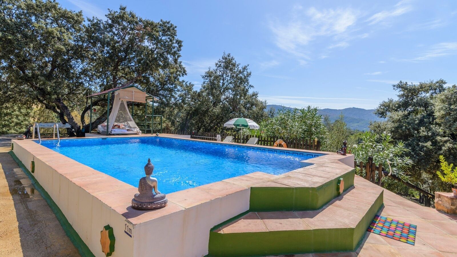 Une piscine rectangulaire avec une statue de Bouddha au centre, entourée d’une terrasse aux couleurs vertes et beiges.