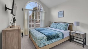 Un dormitorio con cama, mesita de noche, lámpara y una ventana con cortinas.
