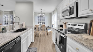 Una cocina moderna con armarios blancos, encimera de granito y electrodomésticos de acero inoxidable.