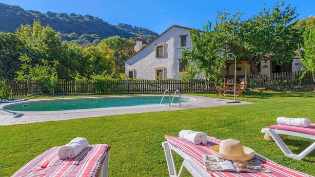 A poolside area with lounge chairs and a pool, surrounded by a wooden fence and greenery. - Molino La Catedral Grazalema by Ruralidays (Cádiz)