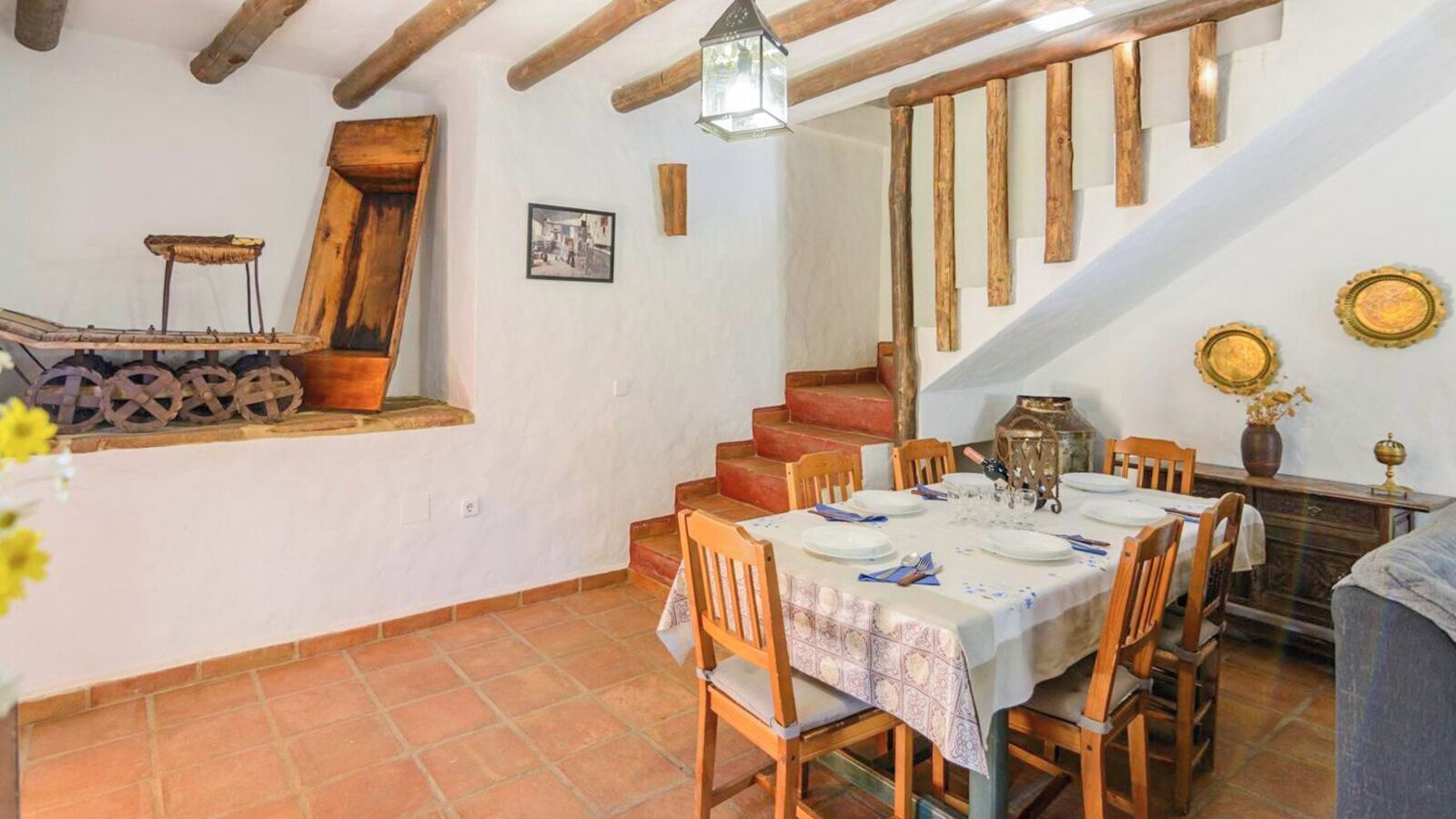 A dining area with a table set for four, wooden chairs, a staircase, and rustic decor.
