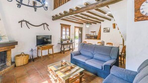 A rustic living room with a blue sofa, a television, a fireplace, and wooden beams on the ceiling. - Molino La Catedral Grazalema by Ruralidays (Cádiz)