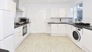 A modern kitchen with white cabinets, a built-in oven, a washing machine, and a window providing natural light. - Townhouse @ 272 Walthall Street Crewe (Crewe)