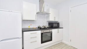 A modern kitchen with white cabinets, a black oven, a microwave, and a stainless steel range hood. - Townhouse @ 272 Walthall Street Crewe (Crewe)