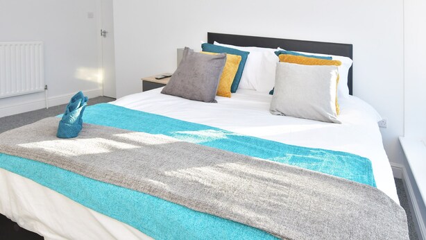 A neatly made bed with a blue and white striped blanket, a grey throw, and multiple pillows in various colors. - Townhouse @ 272 Walthall Street Crewe (Crewe)