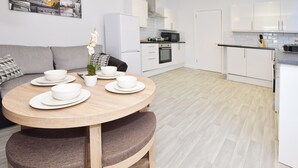 A modern kitchen with white cabinets, a microwave, and a stove. There is a dining table with white bowls and a potted plant. - Townhouse @ 272 Walthall Street Crewe (Crewe)
