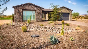 A modern two-story house with a stone facade, a garage, and a landscaped front yard with desert plants. - Rio Verde Home with Stunning Views and a Private Pool (Rio Verde)