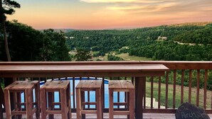 Eine HolzdTerrasse mit drei Hockstühlen und einem Stein, auf dem 'The Perch' steht, mit Blick auf ein bewaldetes Tal.