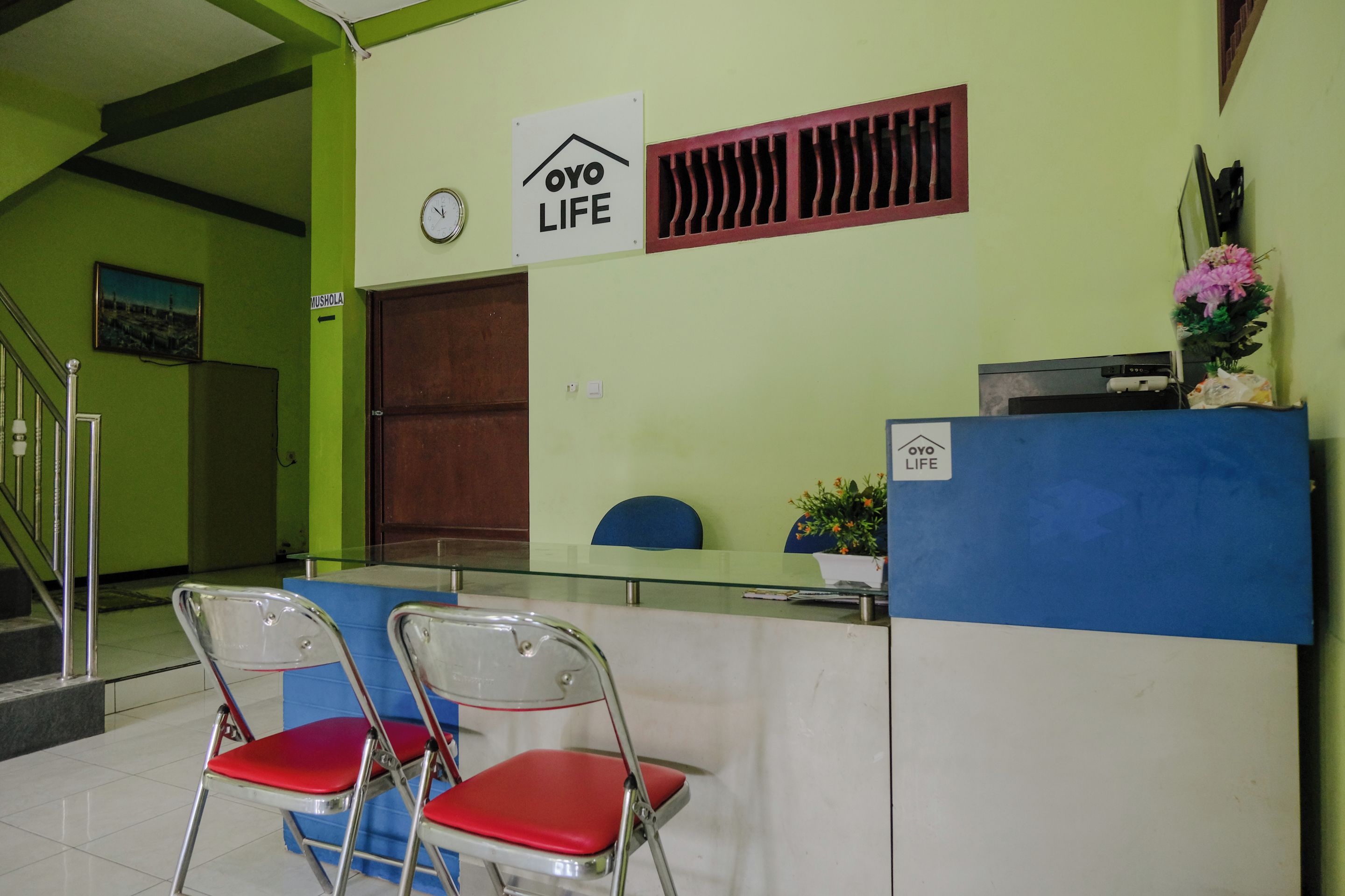 Uma área de recepção com balcão, duas cadeiras vermelhas, um relógio e uma placa com a inscrição 'OYO LIFE'.